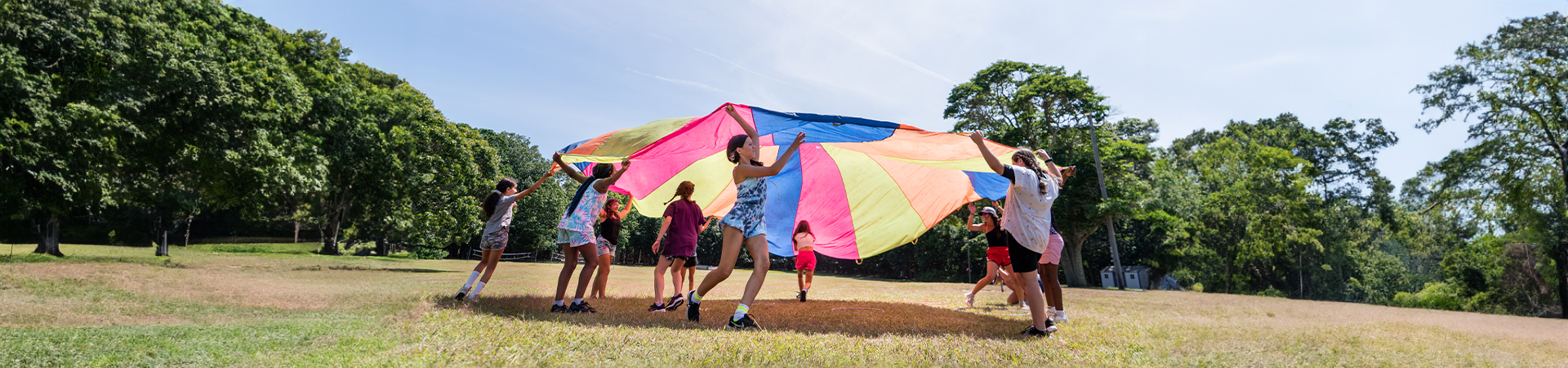  girls outside in the sunshine at camp playing with a parachute 