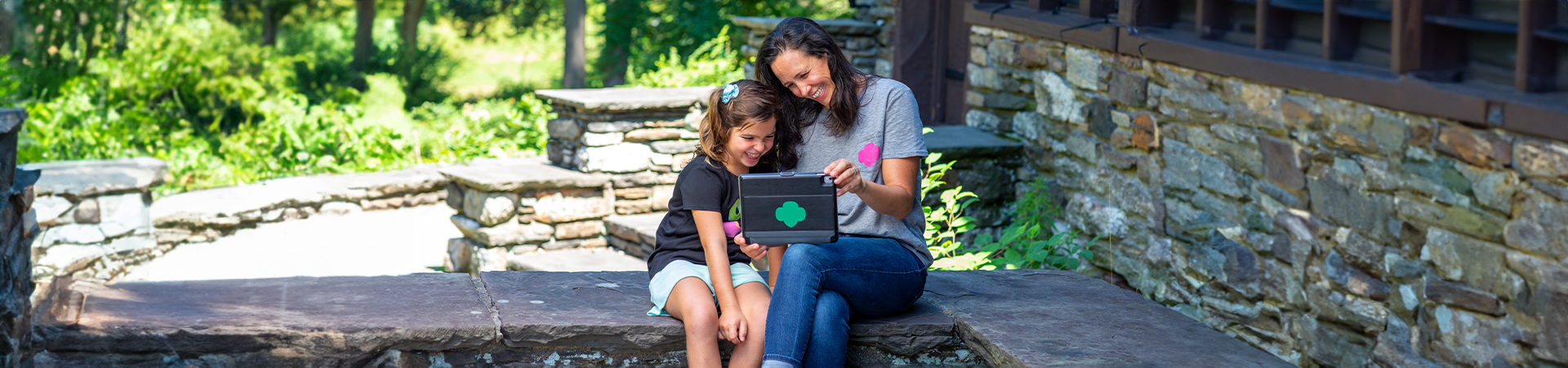  mother and daughter Girl Scout sitting outside looking at something on a tablet device 