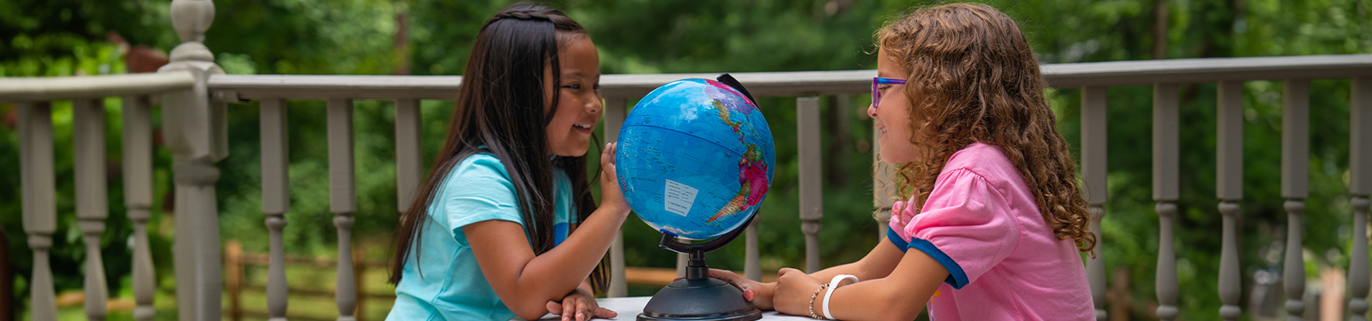  Girl Scouts sitting outside at a table looking at a globe together 