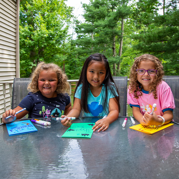 Girls smiling as they work on an activity at a table outside