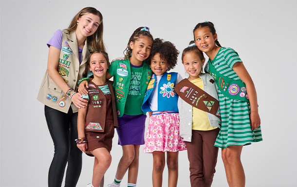 Girl Scouts of various ages in uniform standing together and smiling for a photo