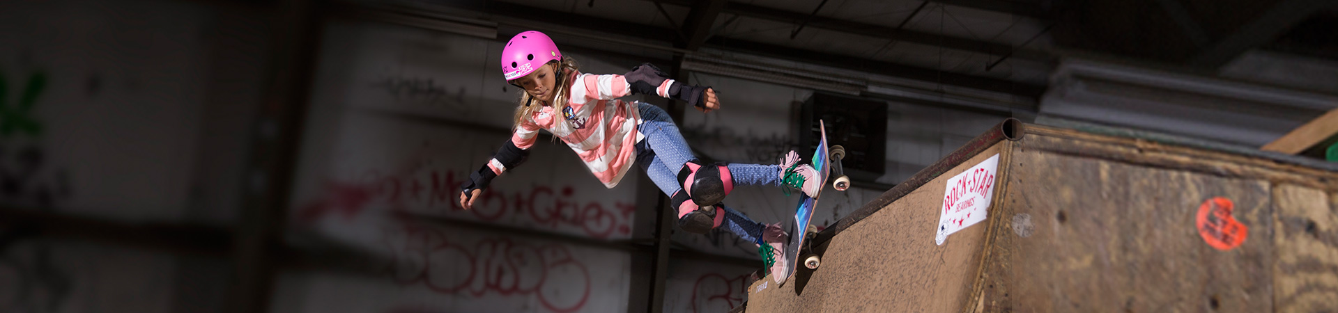  young girl skateboarding on ramp doing trick with pink helmet 