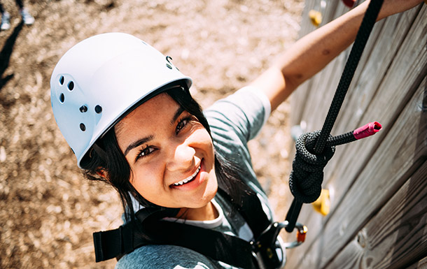 smiling Girl Scout scales an outdoor climbing wall