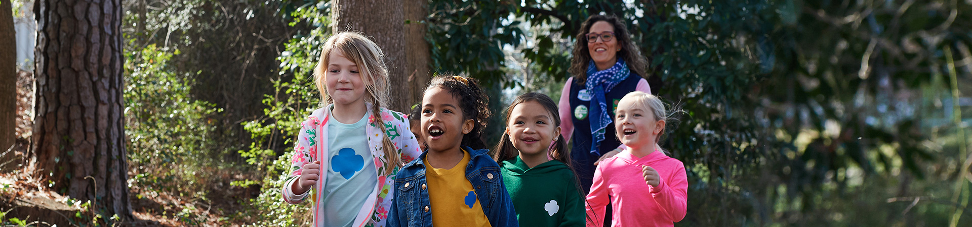  group of Girl Scouts walking outdoors with adult volunteer 