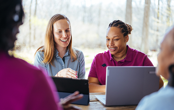 group of diverse adult women sitting outside looking at laptops