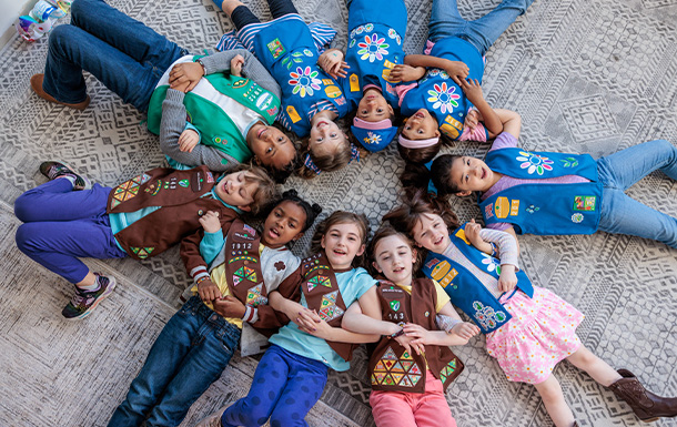 Girl Scouts arm in arm in a circle on the floor together at a troop meeting
