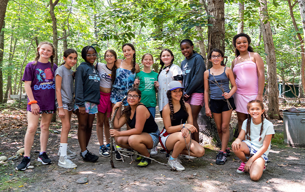 Girl Scouts stand together under the shade of trees at camp