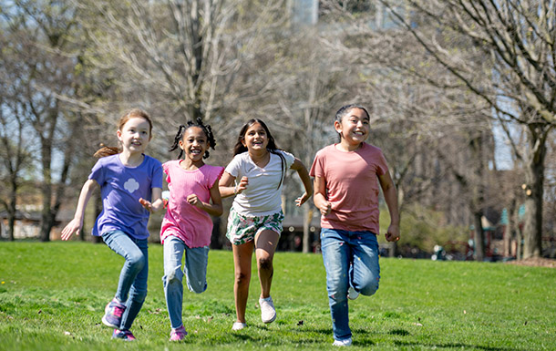 Girl Scouts outside running across a field in the park on a sunny day