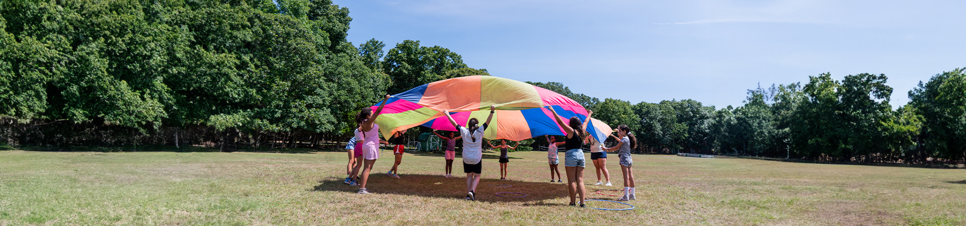  girls outside in a field playing with a colorful parachute 