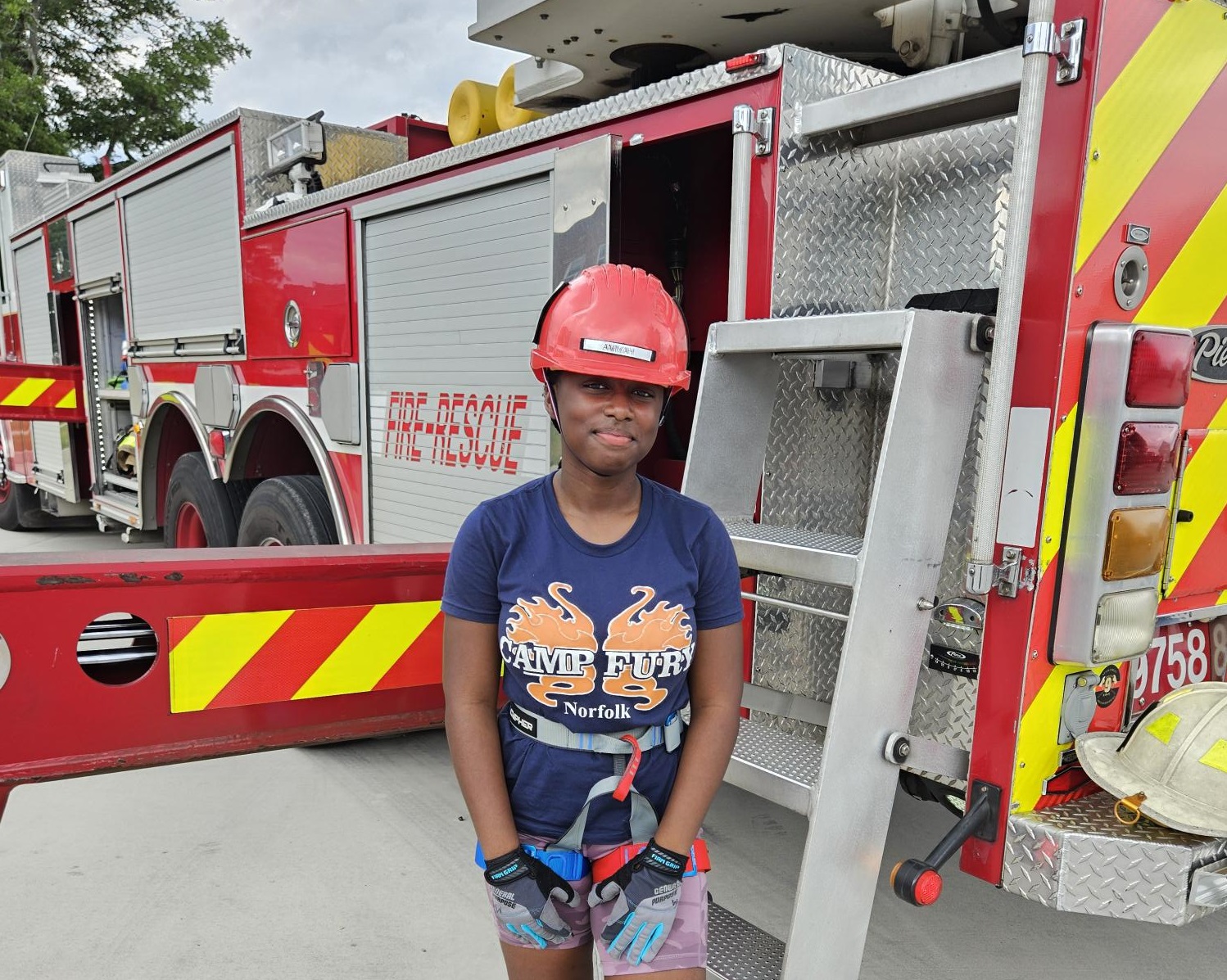 Girl Scout in rappelling gear next to a fire engine at Camp Fury