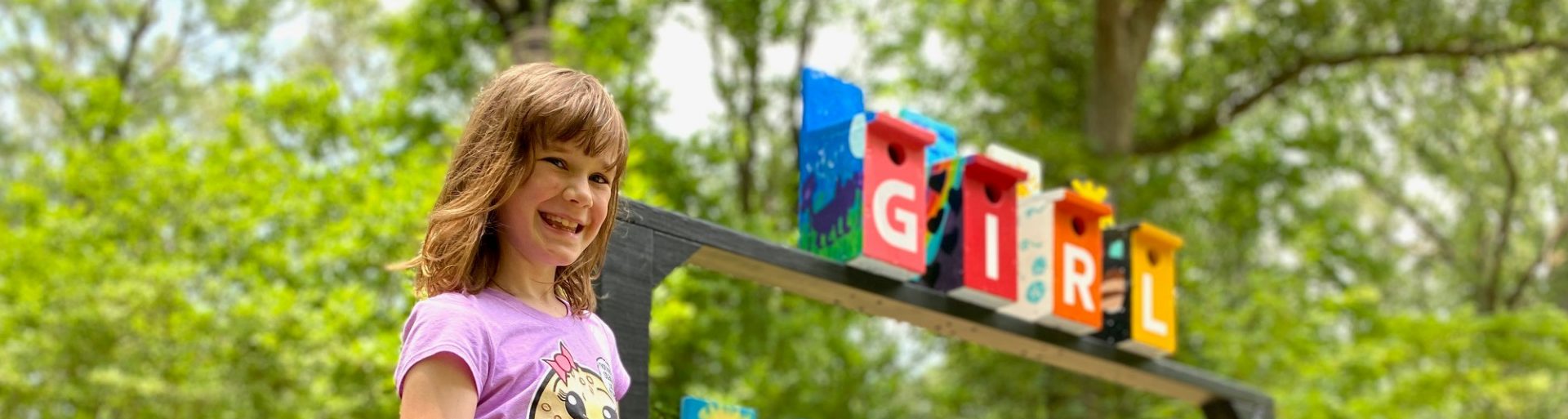  A Girl Scout stands next to the "Rainbow Retreat" birdhouse installation at Norfolk Botanical Garden’s 2023 “Beakitecture” exhibit. 