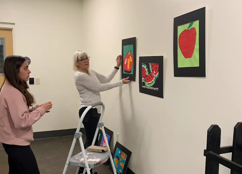 Girl Scout Ambassador Sarah working with staff to hang the artwork