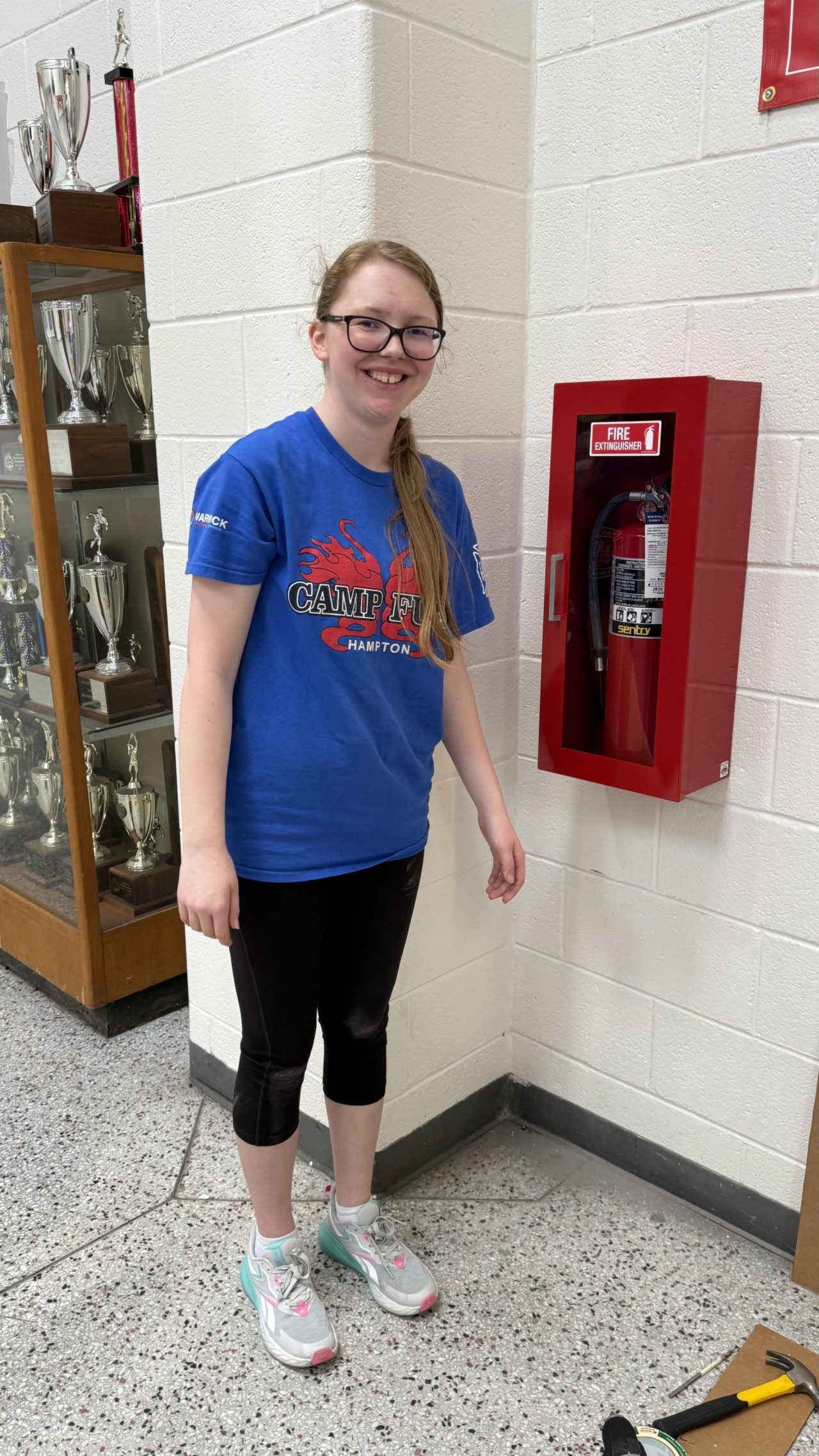 Gold Award Girl Scout Aliya poses next to one of the finished fire extinguisher cabinets she installed