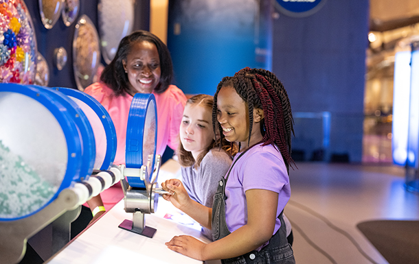 Girl Scouts at a science museum exhibit with adult volunteer