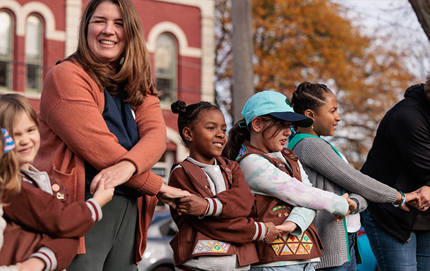 adult volunteers and Girl Scouts stand in a friendship circle outdoors