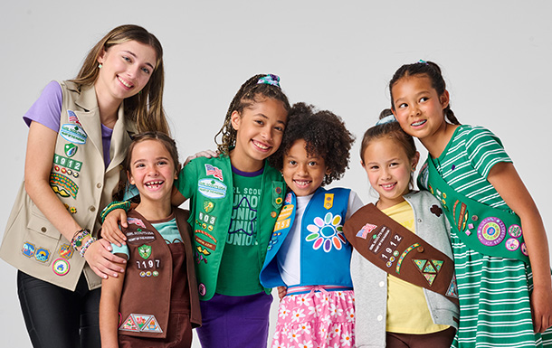 Girl Scouts of various ages in uniform standing together and smiling