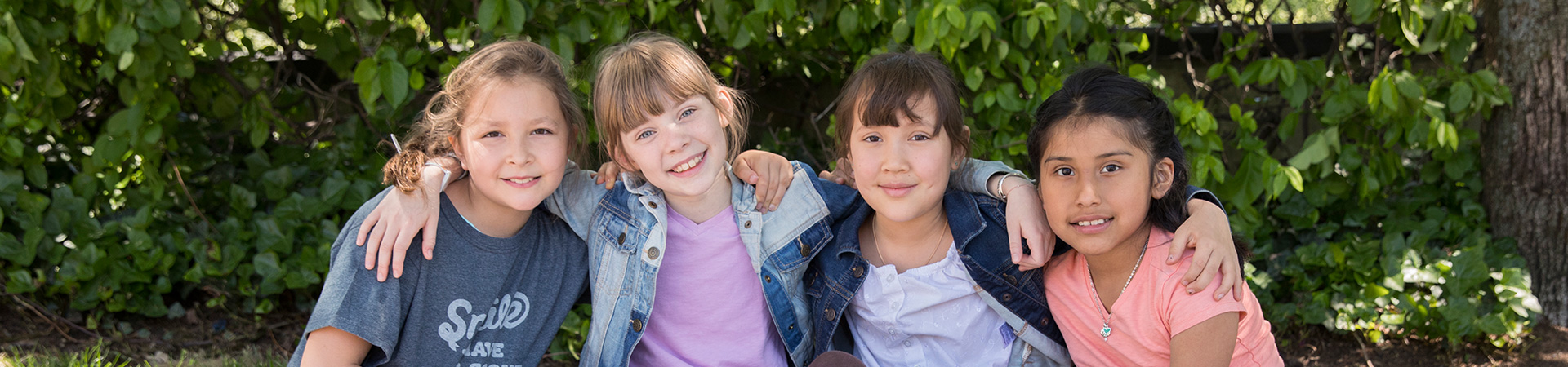  group of girl scouts sitting outdoors, leaning on each other and smiling 