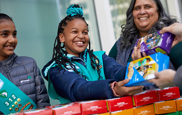 girl scouts selling cookies outside with parent volunteer