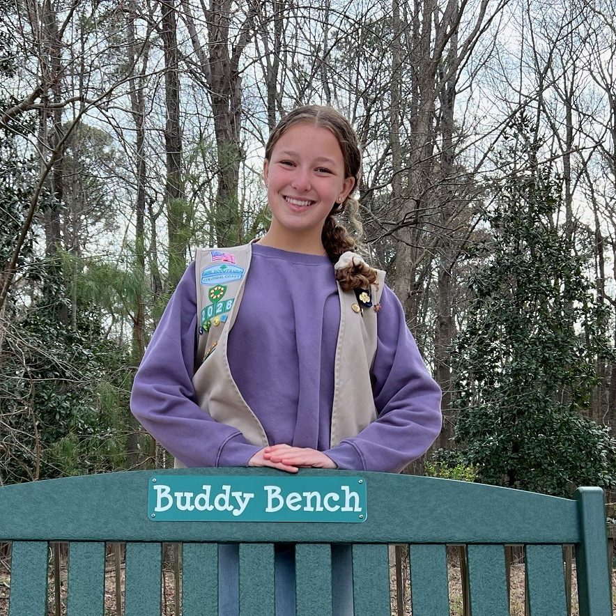 Silver Award Girl Scout wearing uniform vest standing outdoors with bench that was part of her project