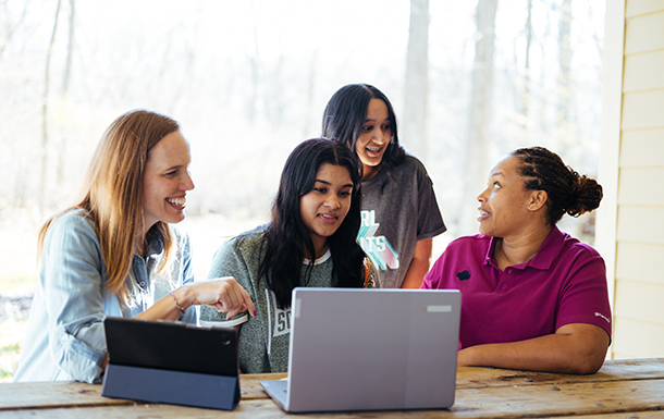 adult volunteers and girl scouts sitting at table outside with their laptops
