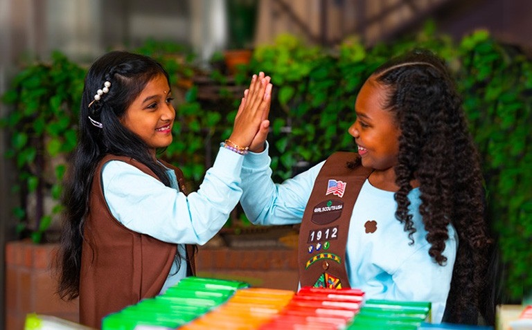 girl scouts giving each other a high five at a cookie booth