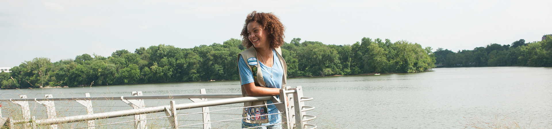  girl scout wearing vest and smiling as she stands at the waterfront 